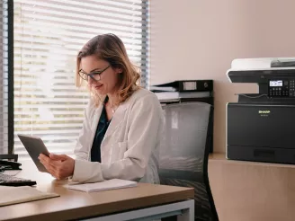 Woman at desk in small office with printer in background