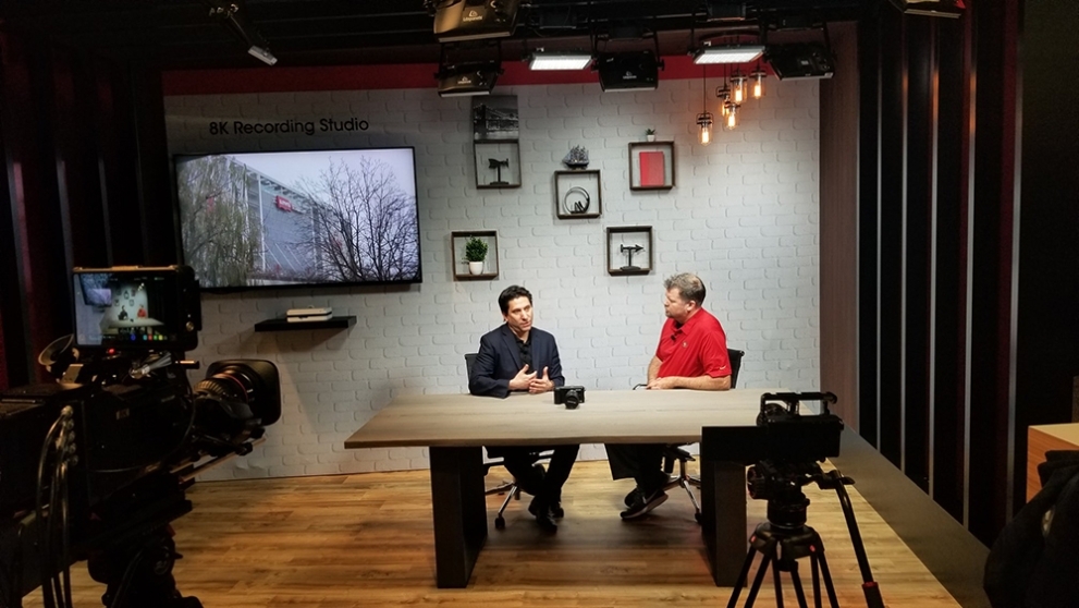 Two men talking at a table in front on 8K screen